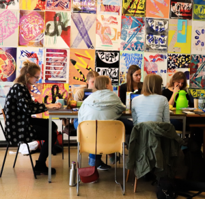 Gruppe von Studenten am Tisch mit bunten Plakaten im Hintergrund.